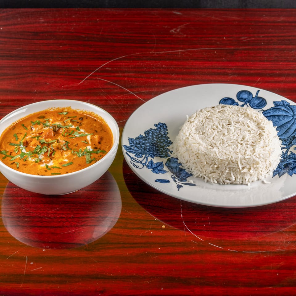 A bowl of Indian butter chicken with cream and cilantro, alongside a plate of white rice.