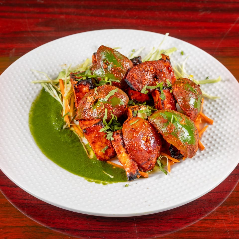 Indian paneer tikka with green bell peppers, cilantro, and a green sauce on a white plate.