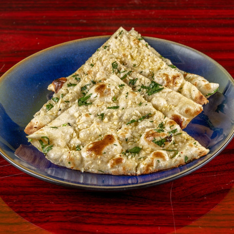 Garlic naan bread, garnished with herbs, served on a blue plate at MITTI FOOD COURT.