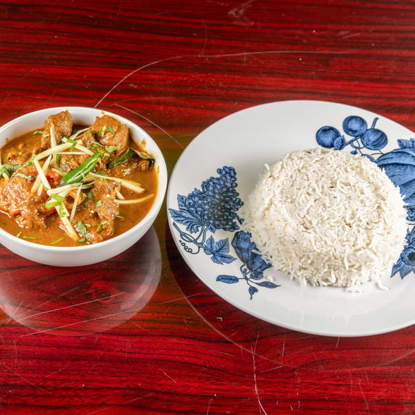 Indian curry with meat and vegetables in a white bowl, served with white rice on a patterned plate.